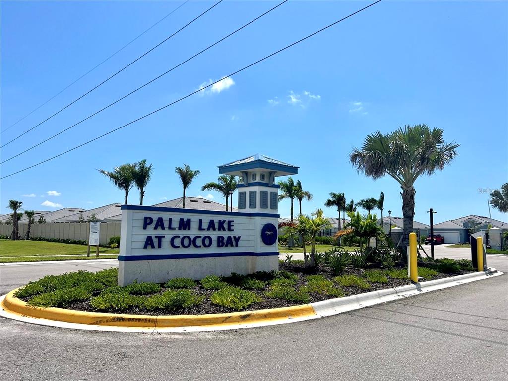 A community entrance sign for Palm Lake at Coco Bay stands on a landscaped corner — 8057 SHORE LAKE DRIVE, ENGLEWOOD, FL