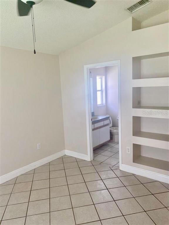A room with tiled floors, a ceiling fan, built-in wall shelves, and an adjoining bathroom — 333 PICCOLO WAY, DAVENPORT, FL
