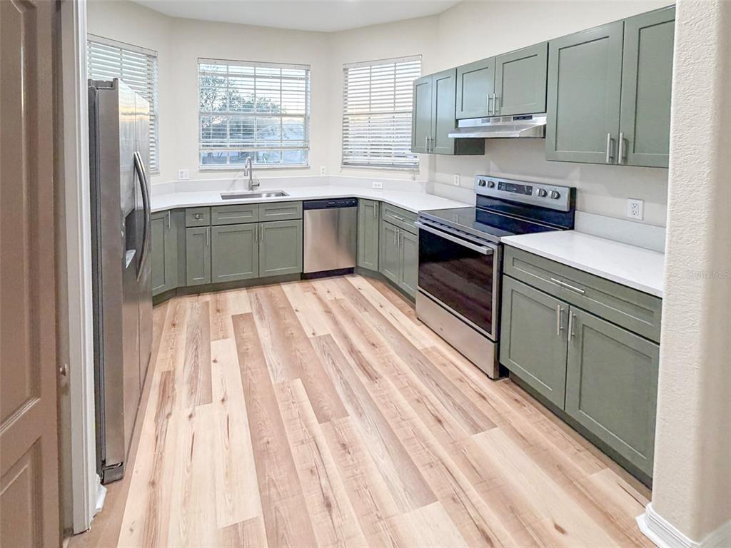 A kitchen features sage green cabinets, stainless steel appliances, white countertops, and light wood flooring — 5014 YELLOWTOP LOOP, LAKELAND, FL