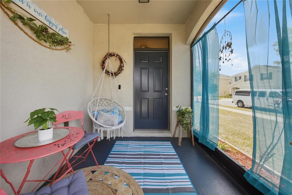 A covered porch features a hanging chair, a pink bistro set, and a striped rug — 10101 MANGROVE WELL ROAD, RUSKIN, FL