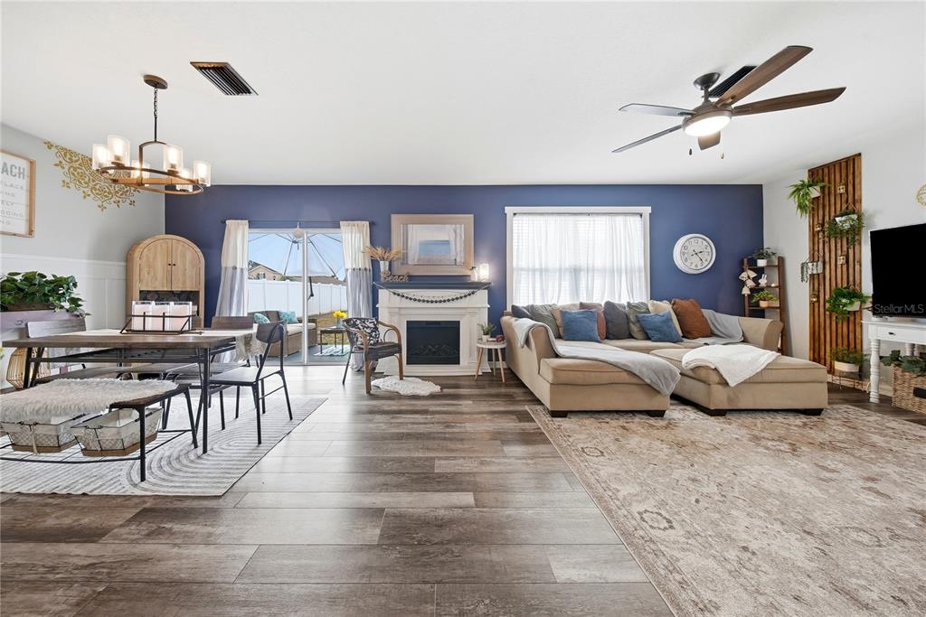 A living and dining room features a blue accent wall, fireplace, and wood-look flooring — 10101 MANGROVE WELL ROAD, RUSKIN, FL