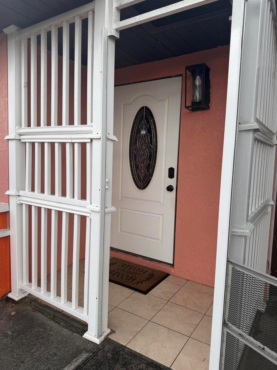 A white front door with an oval glass insert is framed by a white lattice — 1410 NE 14th Terrace, Cape Coral FL 33909, CAPE CORAL, FL
