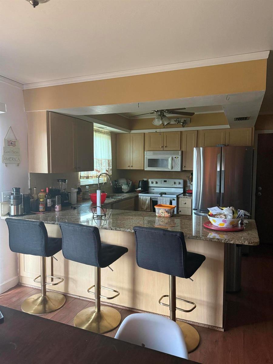 A kitchen with light wood cabinets, granite countertops, a breakfast bar, and stainless steel appliances — 1410 NE 14th Terrace, Cape Coral FL 33909, CAPE CORAL, FL