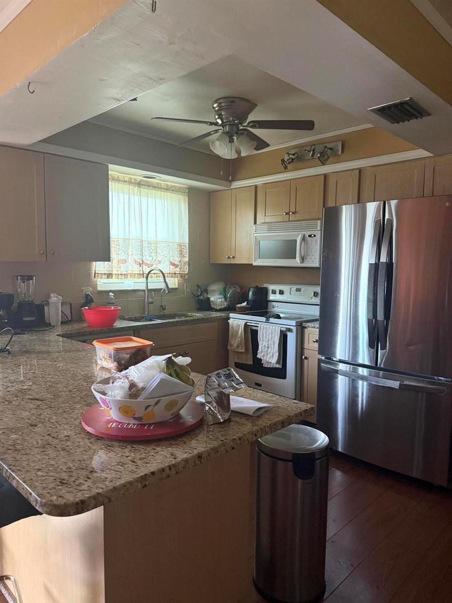 A kitchen features granite countertops, light wood cabinets, stainless steel appliances, and a ceiling fan — 1410 NE 14th Terrace, Cape Coral FL 33909, CAPE CORAL, FL