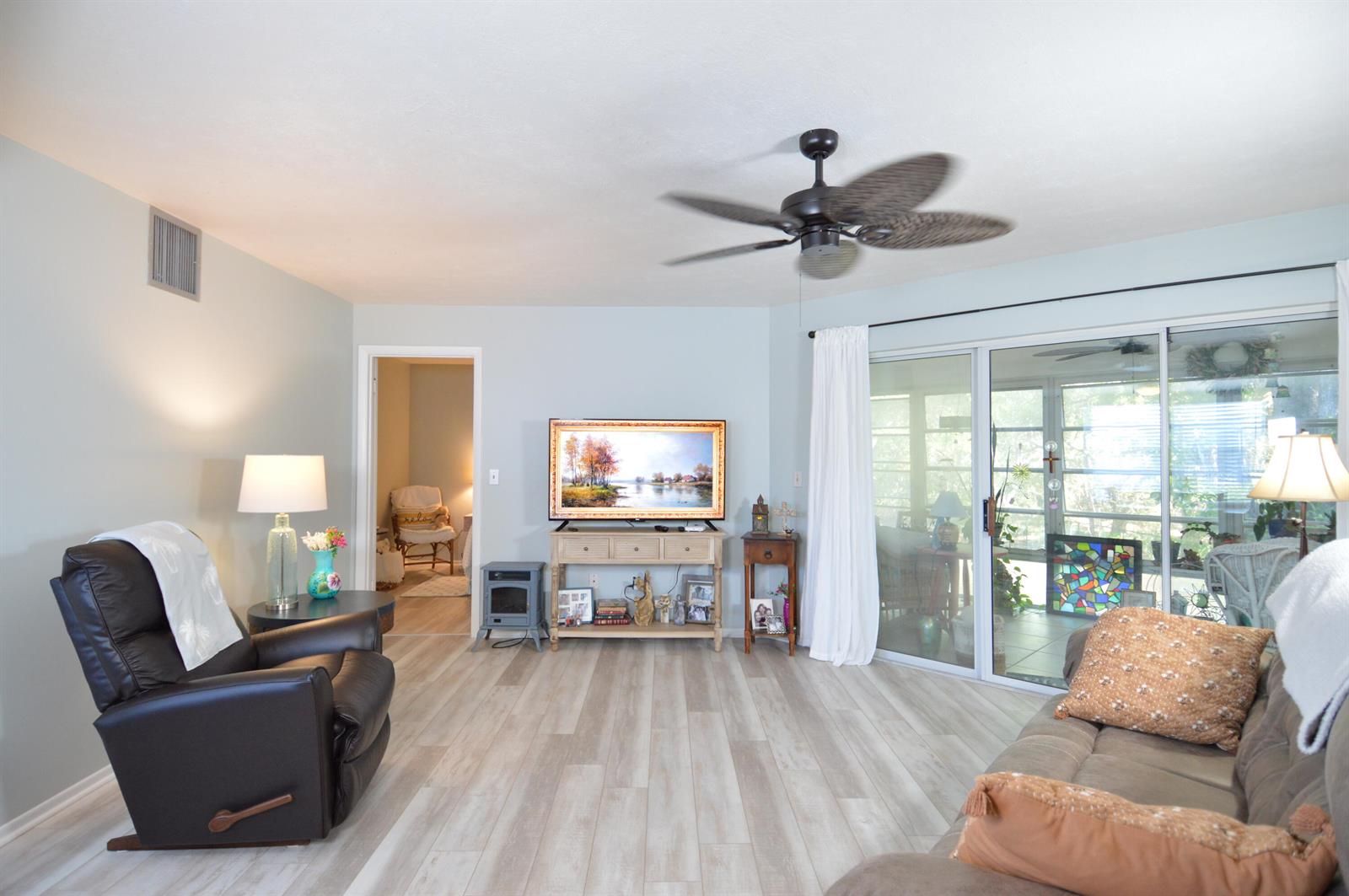 A living room features light wood-look flooring, a ceiling fan, and sliding glass patio doors — 3272 SE Aster Lane # G249, Stuart FL 34994, STUART, FL