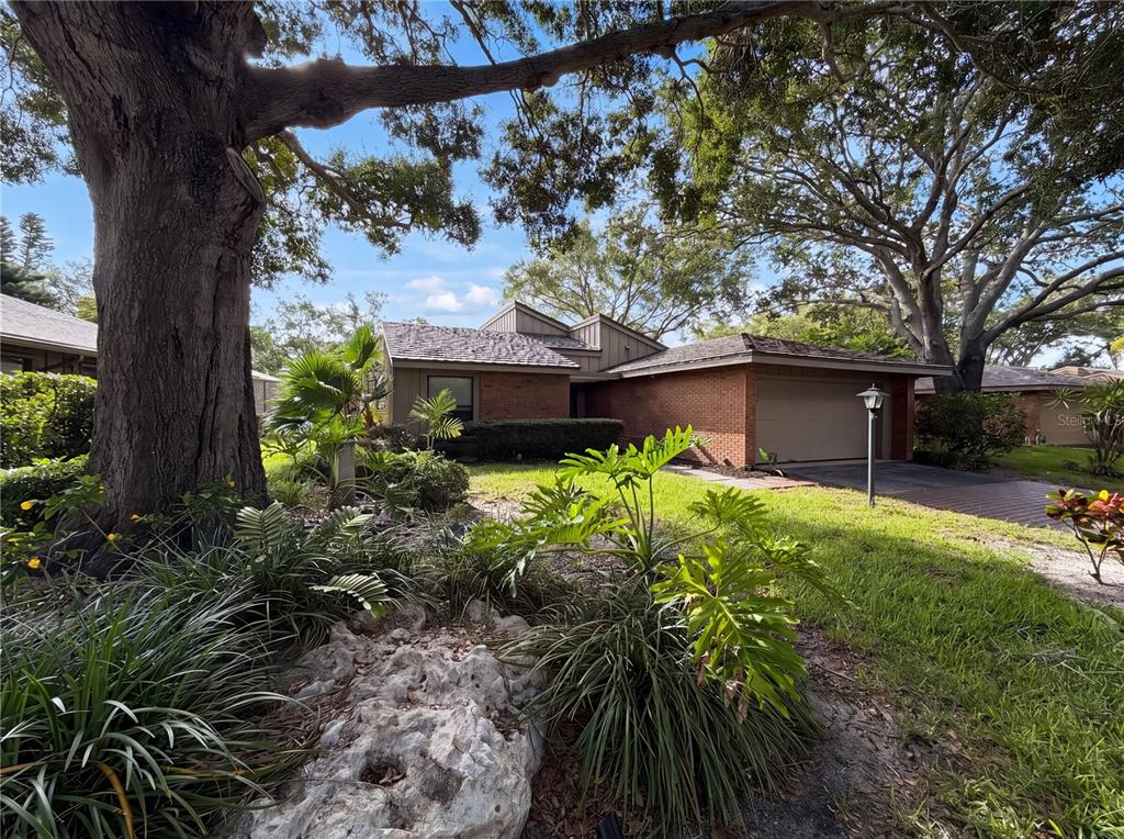 A single-story brick house with a garage is surrounded by large trees and landscaping — 1407 WILLOW OAK CIRCLE UNIT 1407, BRADENTON, FL