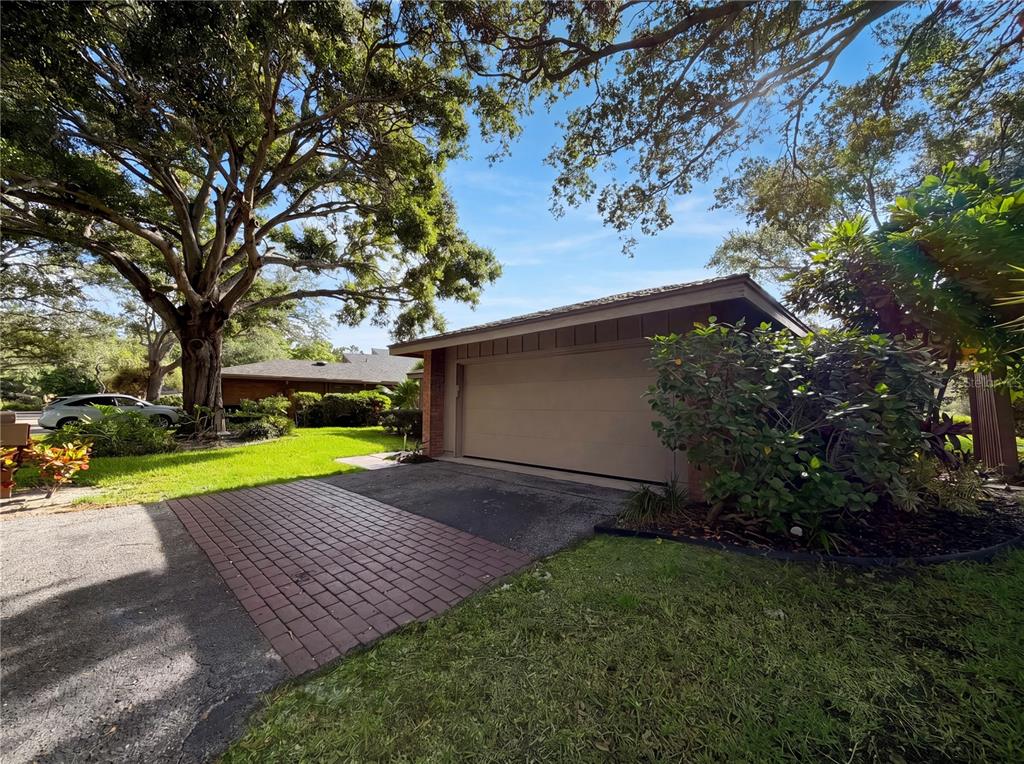 A detached garage with a tan door sits next to a brick-paved driveway and lawn — 1407 WILLOW OAK CIRCLE UNIT 1407, BRADENTON, FL