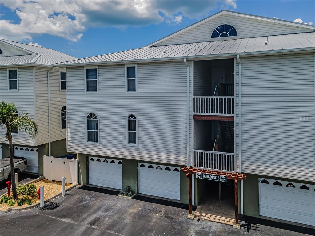 An exterior view of a multi-story residential building with white siding and garage doors — 19829 GULF BOULEVARD UNIT 501, INDIAN SHORES, FL