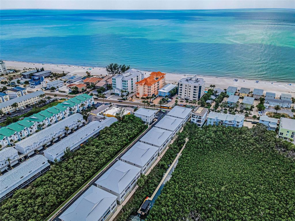 An aerial view shows a coastal residential area with multi-story buildings near a sandy beach — 19829 GULF BOULEVARD UNIT 501, INDIAN SHORES, FL
