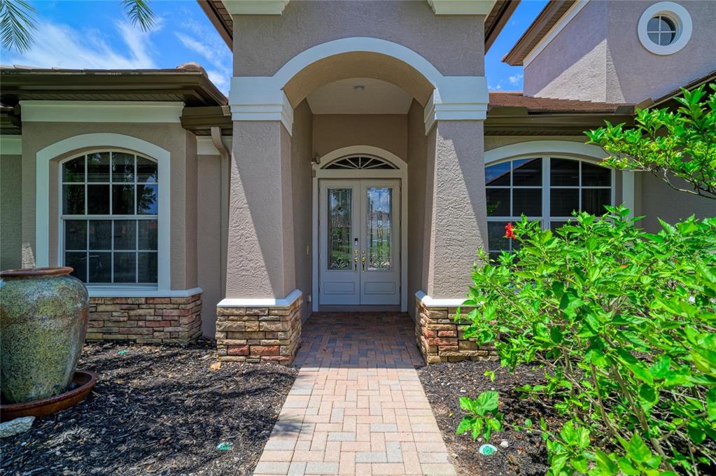 A paved walkway leads to the double front doors of a stucco house with stone accents — 13329 SWALLOWTAIL DRIVE, LAKEWOOD RANCH, FL