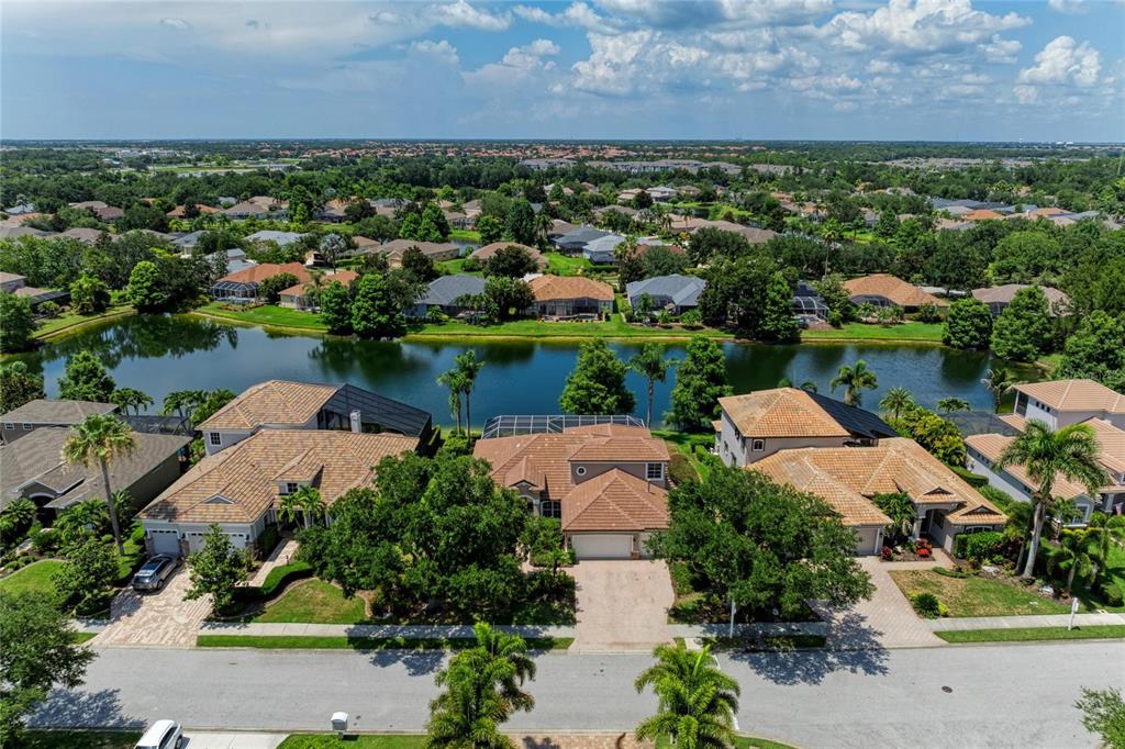 An aerial view shows three suburban houses with tiled roofs situated along a lake — 13329 SWALLOWTAIL DRIVE, LAKEWOOD RANCH, FL