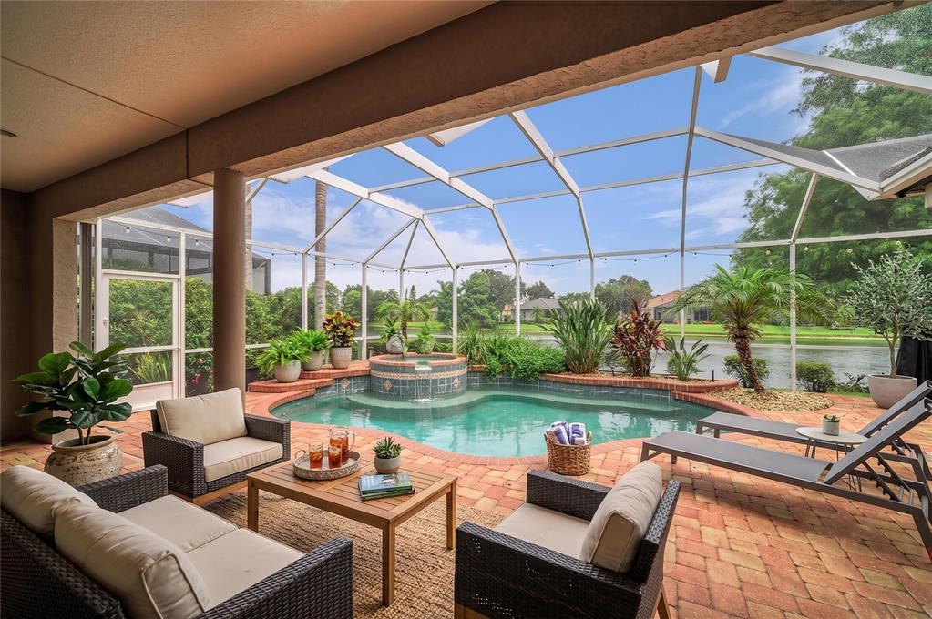A covered patio features a screened-in pool, a hot tub, and outdoor furniture overlooking water — 13329 SWALLOWTAIL DRIVE, LAKEWOOD RANCH, FL