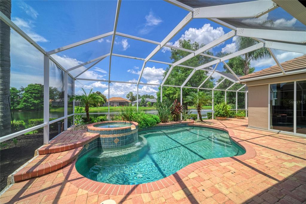 A screened-in pool and spa area with brick pavers overlooking a lake — 13329 SWALLOWTAIL DRIVE, LAKEWOOD RANCH, FL