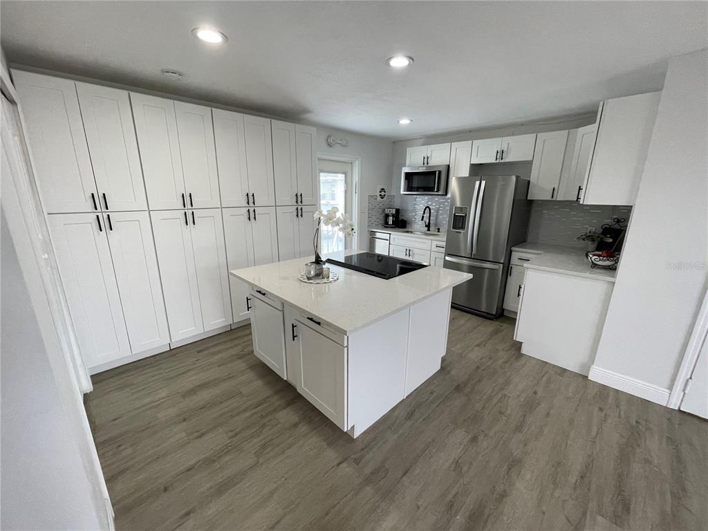 A modern kitchen features white cabinetry, a central island with a cooktop, and wood-look flooring — 151 N ORLANDO AVENUE UNIT 238, WINTER PARK, FL