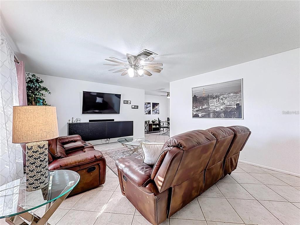 A living room features brown leather sofas, a television, and tile flooring — 1905 HUGHEY STREET, KISSIMMEE, FL