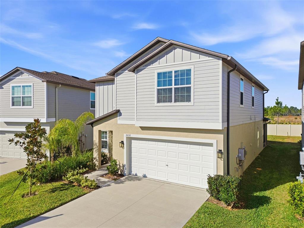 A two-story suburban house with light-colored siding, a single-car garage, and a front lawn — 35132 ACKLEY TRACE, ZEPHYRHILLS, FL