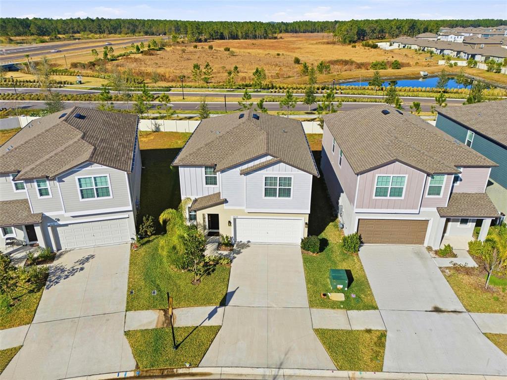An aerial view shows three suburban houses with driveways and lawns facing a road — 35132 ACKLEY TRACE, ZEPHYRHILLS, FL