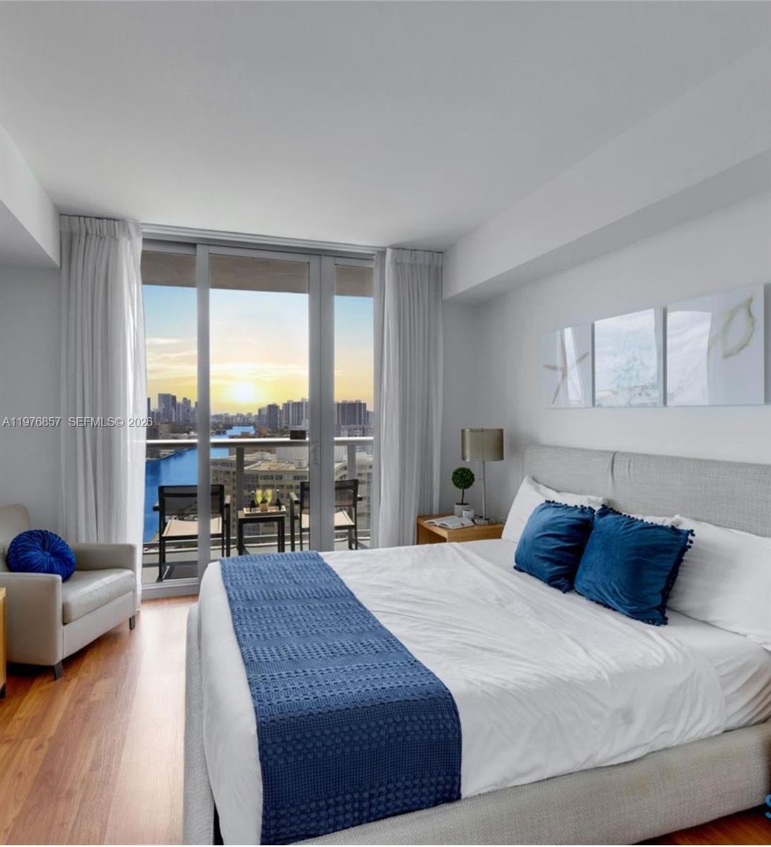 A bedroom features a bed with blue accents, a gray armchair, and a balcony with water views — 2602 E Hallandale Beach Blvd # R3009, Hallandale Beach FL 33009, HALLANDALE BEACH, FL