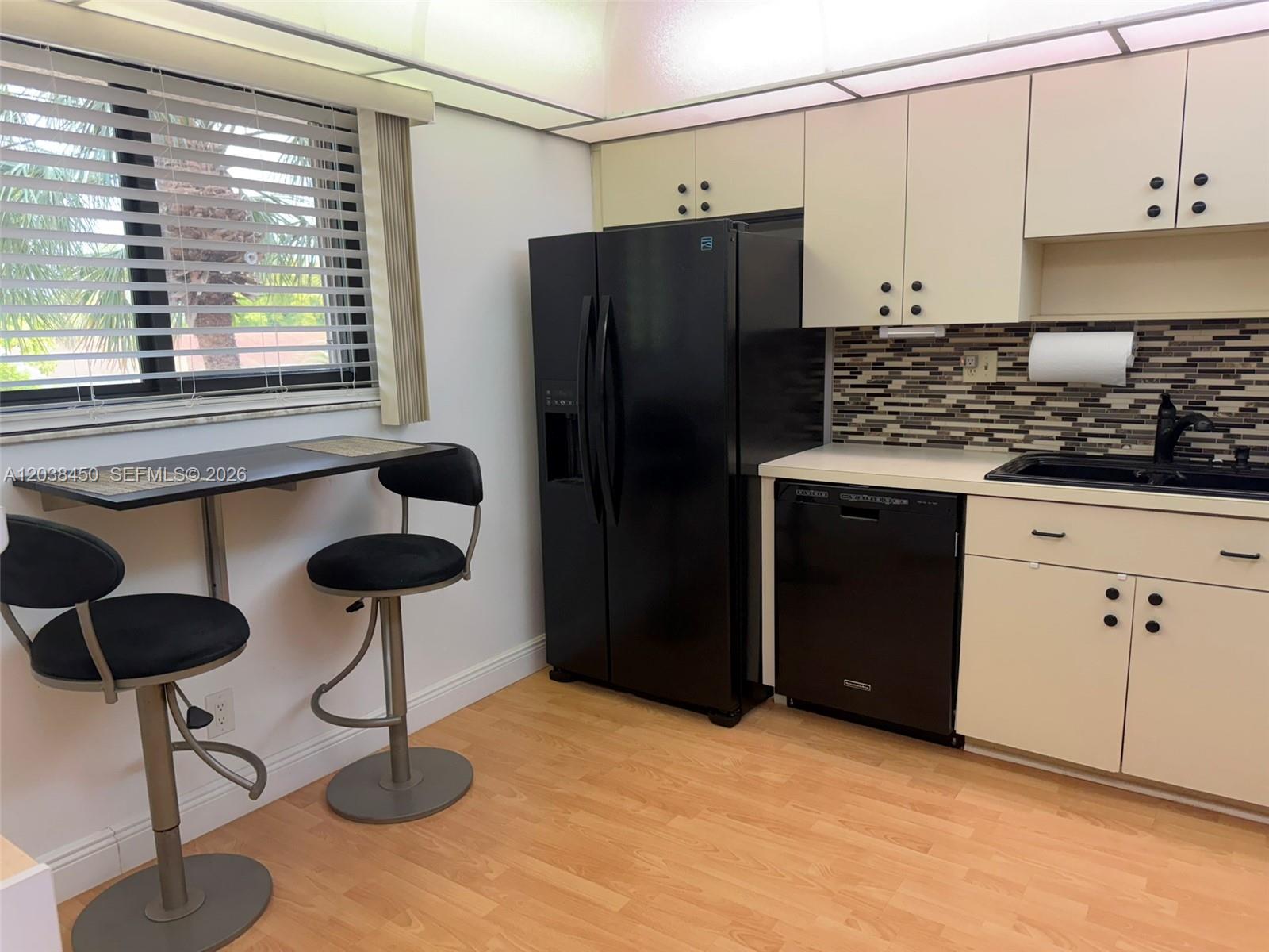 A kitchen features light-colored cabinets, a black refrigerator, a dishwasher, and a small breakfast bar — 4960 E Sabal Palm Blvd # 308, Tamarac FL 33319, TAMARAC, FL