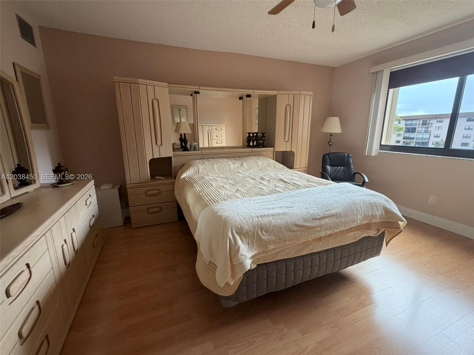 A bedroom features a light wood headboard unit with mirrors, a bed, and laminate flooring — 4960 E Sabal Palm Blvd # 308, Tamarac FL 33319, TAMARAC, FL