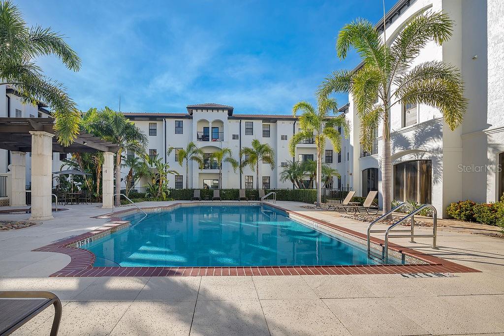 A rectangular swimming pool sits in a courtyard surrounded by multi-story apartment buildings and palm trees — 5550 E MICHIGAN STREET UNIT 2114, ORLANDO, FL