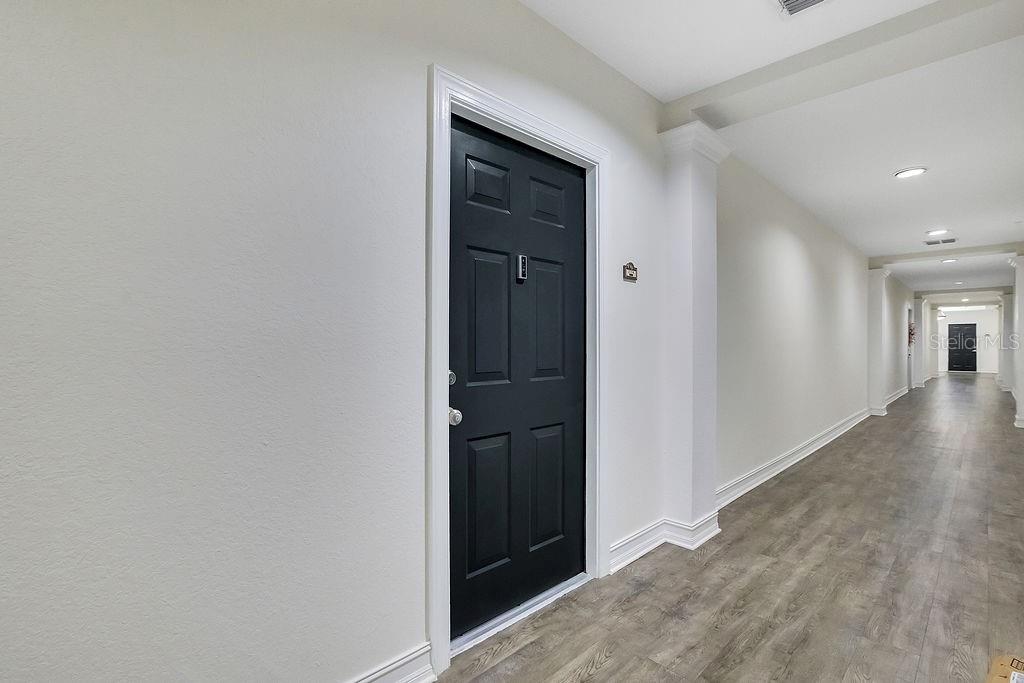 A black door with a silver handle stands in a long, light-colored hallway — 5550 E MICHIGAN STREET UNIT 2114, ORLANDO, FL