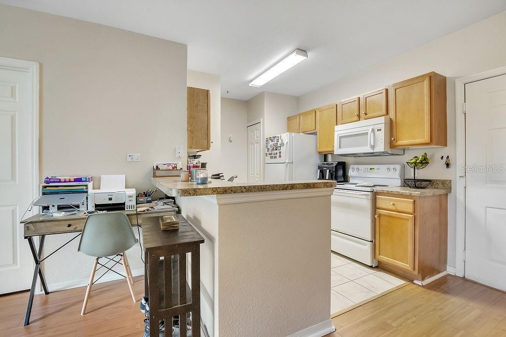 A kitchen with light wood cabinets, white appliances, and a breakfast bar with a desk — 5550 E MICHIGAN STREET UNIT 2114, ORLANDO, FL