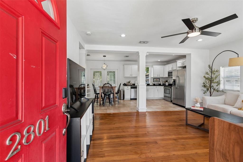 A red front door opens into an open-concept living area with hardwood floors and kitchen — 2801 S MANHATTAN AVENUE, TAMPA, FL