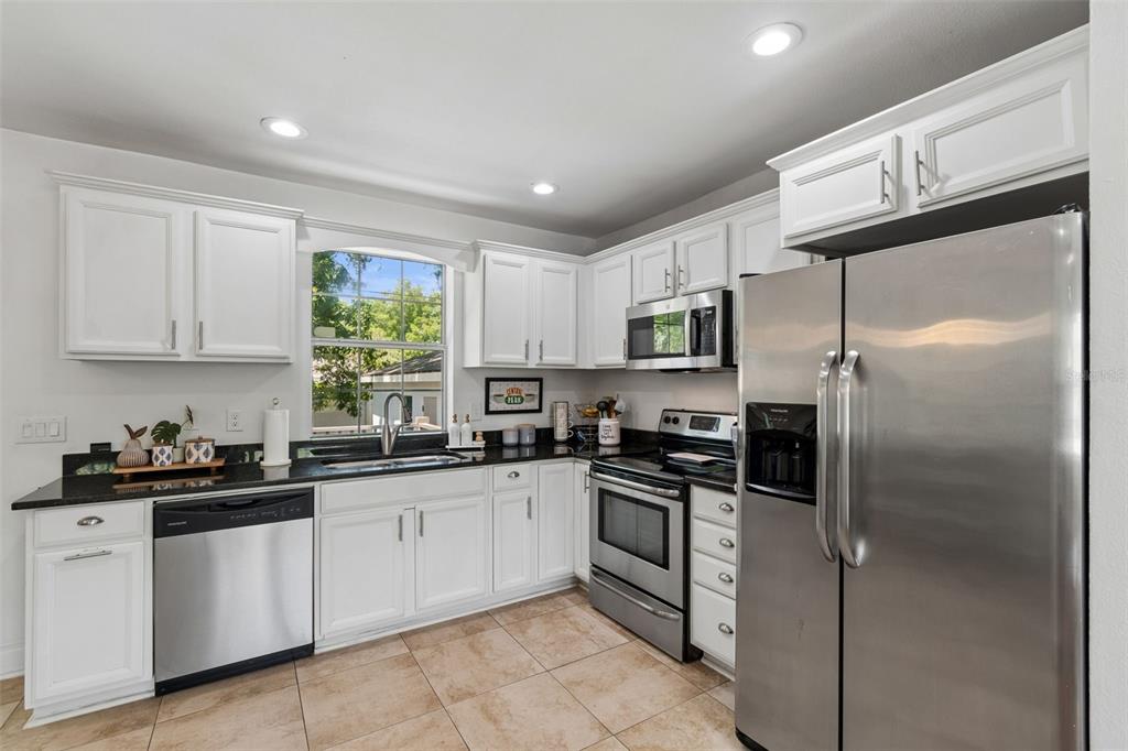 A kitchen features white cabinets, black countertops, stainless steel appliances, and tile flooring — 2801 S MANHATTAN AVENUE, TAMPA, FL