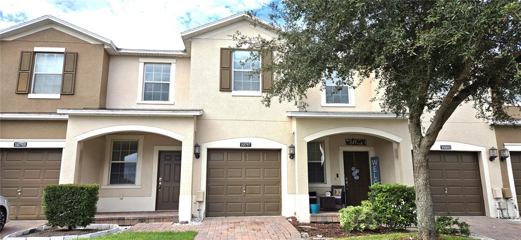 A row of three attached townhouses with tan stucco exteriors, brown garage doors, and arched entryways — 10797 SAVANNAH LANDING CIRCLE, ORLANDO, FL