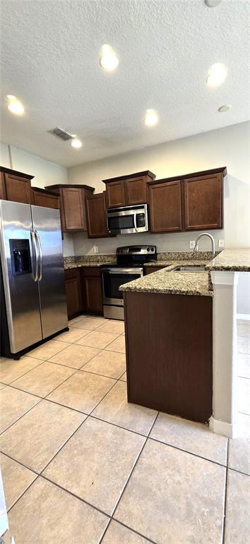 A kitchen features dark wood cabinets, granite countertops, stainless steel appliances, and tile flooring — 10797 SAVANNAH LANDING CIRCLE, ORLANDO, FL