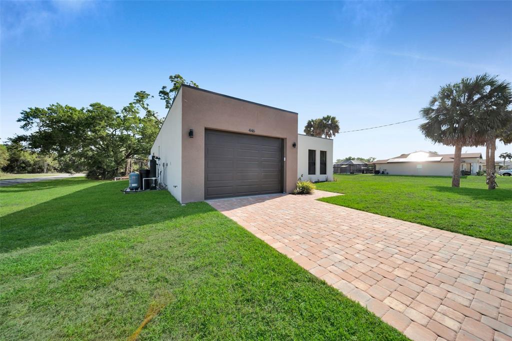 A modern single-story building with a garage door and a paved driveway on a lawn — 446 SKYLAND LANE, PORT CHARLOTTE, FL