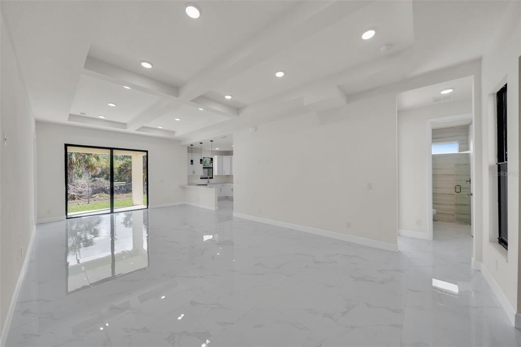 An open-concept living area features white marble-look tile flooring, a coffered ceiling, and sliding doors — 446 SKYLAND LANE, PORT CHARLOTTE, FL