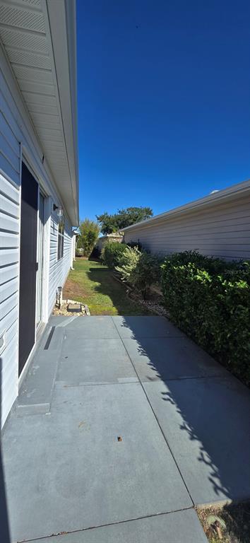 A concrete patio sits between the side of a house and a neighboring wall — 3489 CAMBRIA CIRCLE, THE VILLAGES, FL