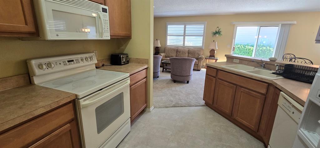A kitchen with white appliances and wood cabinets opens into a carpeted living area — 3489 CAMBRIA CIRCLE, THE VILLAGES, FL