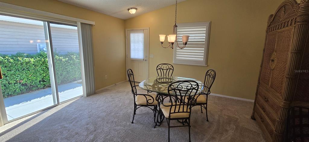 A dining area features a glass table, four metal chairs, carpeted floors, and sliding doors — 3489 CAMBRIA CIRCLE, THE VILLAGES, FL