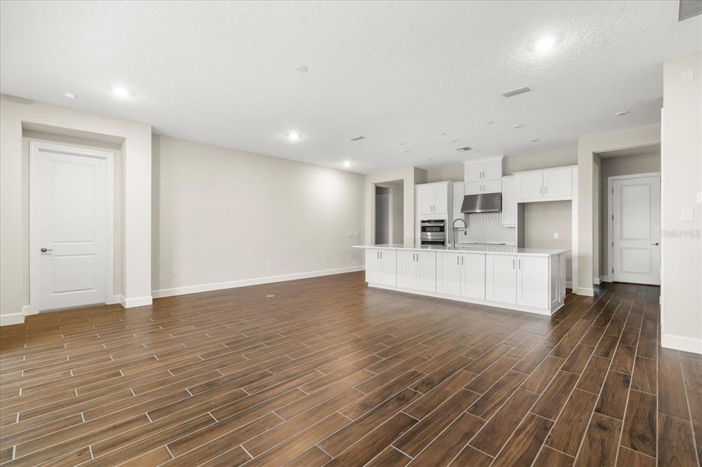 A spacious room with wood-look tile flooring, white kitchen cabinetry, and a large center island — 5683 NEVIS TERRACE, KISSIMMEE, FL
