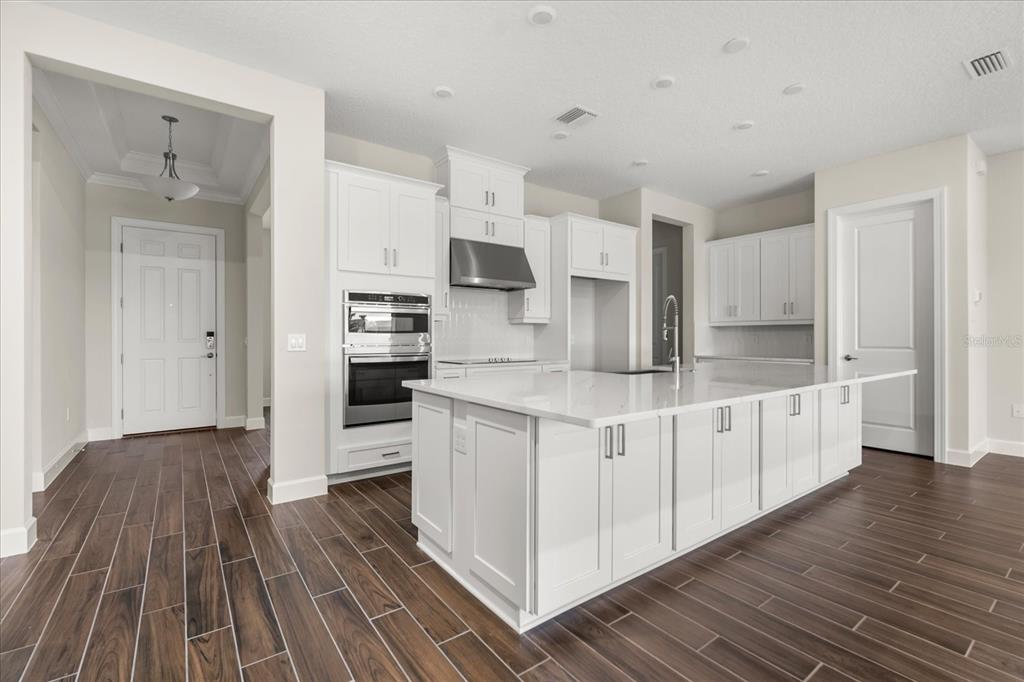 A modern kitchen features white cabinetry, a large center island, and dark wood-look tile flooring — 5683 NEVIS TERRACE, KISSIMMEE, FL