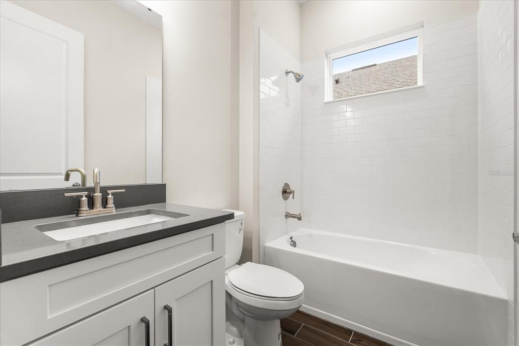 A bathroom features a white vanity with a dark countertop, a toilet, and a tub-shower — 5683 NEVIS TERRACE, KISSIMMEE, FL