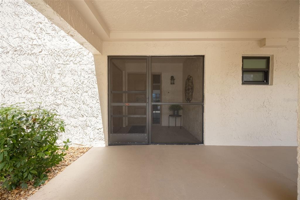 A covered patio features a screen door, a small window, and a nearby green bush — 3 PIRATES LANE UNIT 32A, PUNTA GORDA, FL