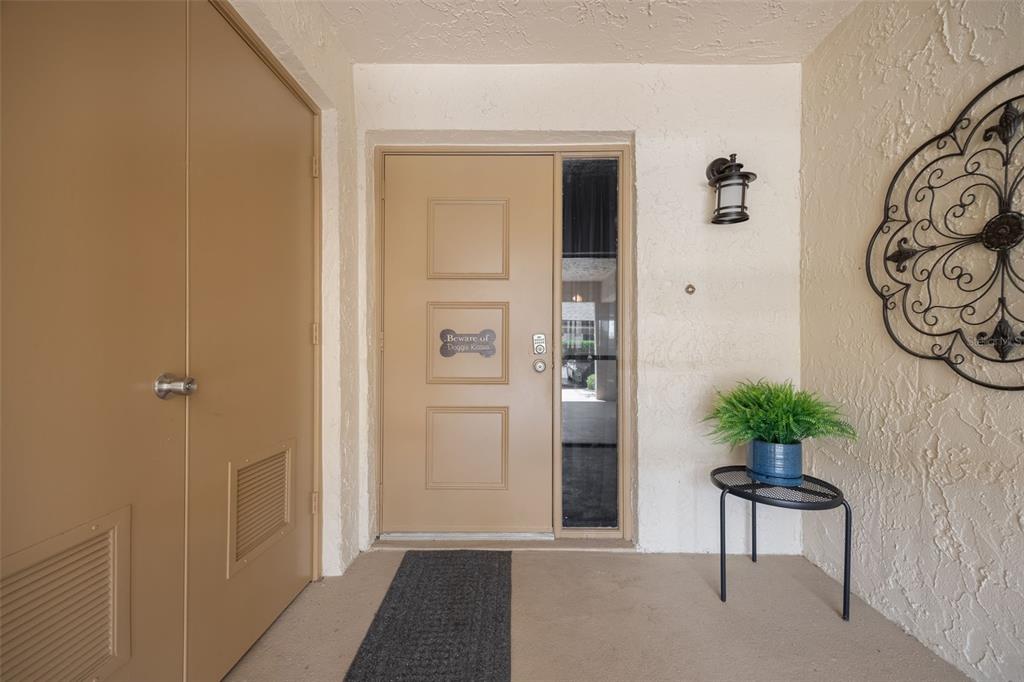 A tan front door with a side window and a small plant on a metal stand — 3 PIRATES LANE UNIT 32A, PUNTA GORDA, FL