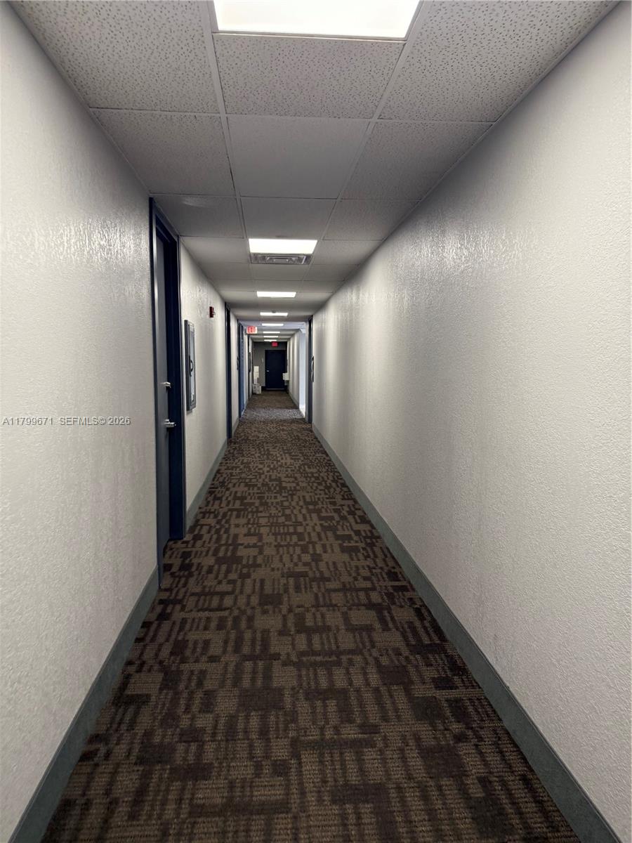 A long, narrow indoor hallway features patterned brown carpeting, white walls, and recessed ceiling lights — 8955 SW 87th Ct # 101, Miami FL 33176, MIAMI, FL