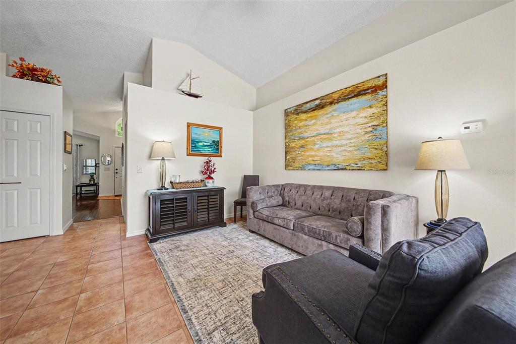 A living room features a grey tufted sofa, a dark wood cabinet, and tile flooring — 2936 MOORCROFT CT, ORLANDO, FL