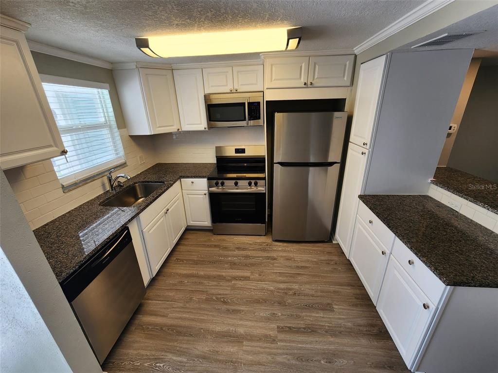 A kitchen features white cabinets, granite countertops, stainless steel appliances, and wood-look flooring — 701 1ST STREET UNIT 2, INDIAN ROCKS BEACH, FL