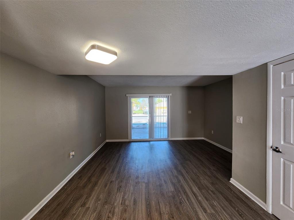 An empty room features dark wood-look flooring, gray walls, a ceiling light, and sliding glass doors — 701 1ST STREET UNIT 2, INDIAN ROCKS BEACH, FL
