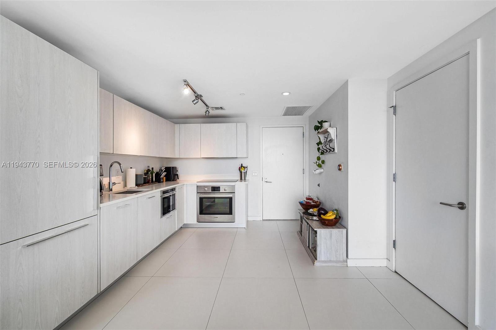 A modern kitchen features light wood cabinetry, stainless steel appliances, and large gray floor tiles — 501 NE 31st St # 3009, Miami FL 33137, MIAMI, FL