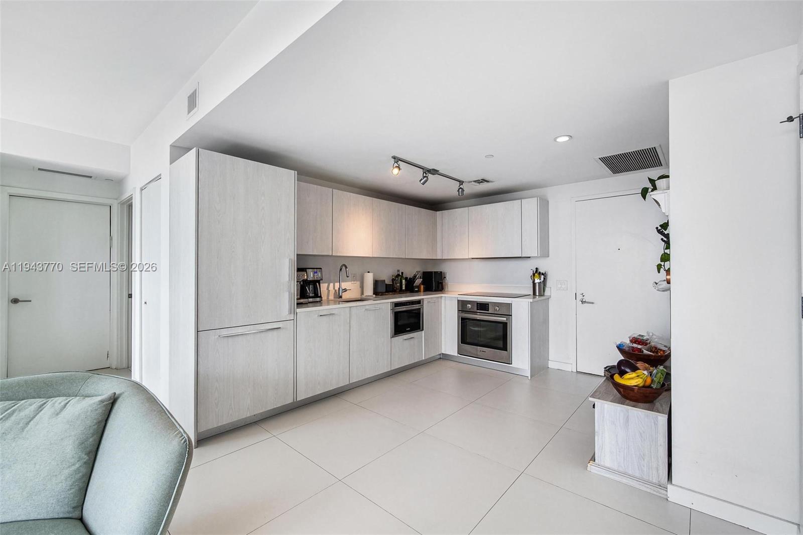 A modern kitchen features light wood cabinetry, stainless steel appliances, and large white floor tiles — 501 NE 31st St # 3009, Miami FL 33137, MIAMI, FL
