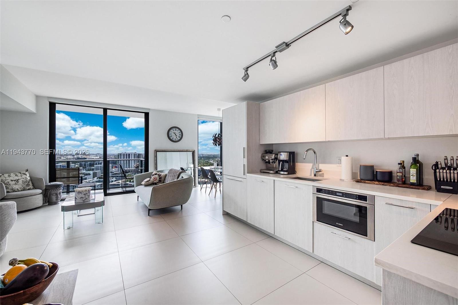 A modern kitchen with light wood cabinetry and stainless steel appliances opens to a living area — 501 NE 31st St # 3009, Miami FL 33137, MIAMI, FL