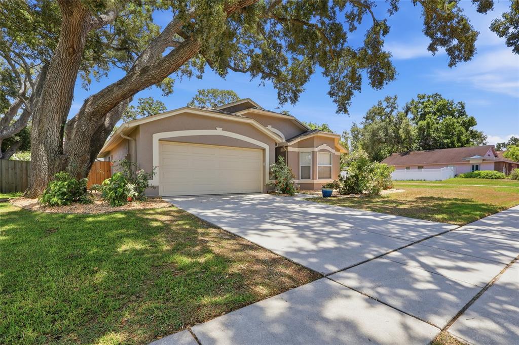 A tan single-story house with a two-car garage and a large oak tree in front — 5724 ERHARDT DRIVE, RIVERVIEW, FL