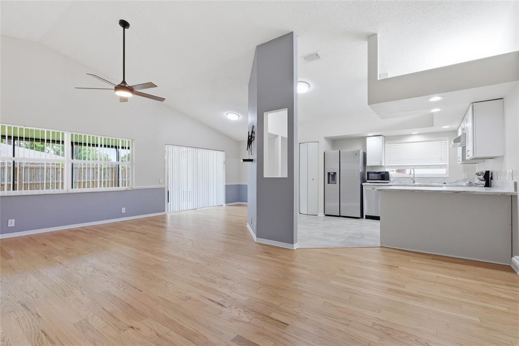 An open-concept living room with hardwood floors, a gray accent wall, and an adjacent kitchen — 5724 ERHARDT DRIVE, RIVERVIEW, FL